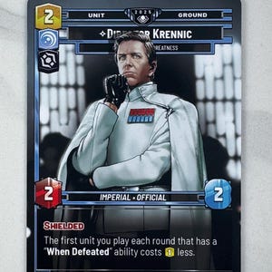 Puede incluir: Una tarjeta coleccionable con el Director Krennic de Star Wars. La tarjeta muestra al personaje con uniforme blanco. El texto incluye "IMPERIAL OFFICIAL" y detalles del juego. La tarjeta tiene un borde negro y es para un juego de cartas.