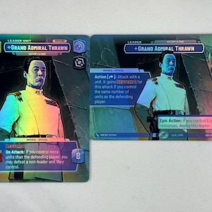 May include: Two holographic trading cards featuring Grand Admiral Thrawn in a white uniform. The cards display game text, including 'Action' and 'Epic Action' abilities, with blue and purple accents. The character is depicted against a dark background.