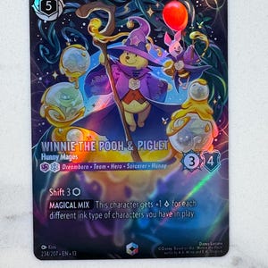 Könnte beinhalten: Eine Disney Lorcana Sammelkarte mit Winnie Puuh und Ferkel als Honigmagier. Die Karte hat ein holografisches Finish, kostet 5 und enthält den Text Winnie the Pooh & Piglet, Hunny Mages, Dreamborn, Team, Hero, Sorcerer, Hunny und Magical Mix.