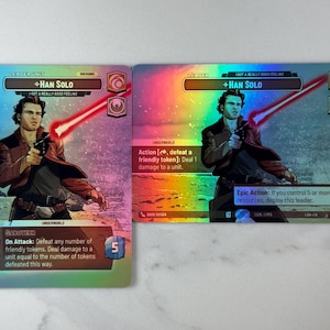 May include: Two holographic trading cards featuring Han Solo from Star Wars. The cards have a rainbow sheen and depict Han Solo holding a blaster and a lightsaber. Text includes "Han Solo" and game instructions.