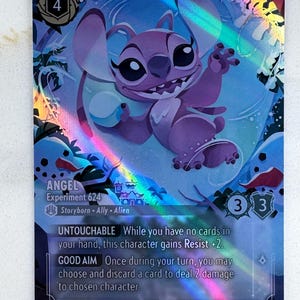May include: A holographic trading card featuring Angel, Experiment 624, from Disney Lorcana. The card has a purple and blue color scheme with a rainbow sheen. Angel is depicted smiling. The card includes text such as "Untouchable" and "Good Aim".
