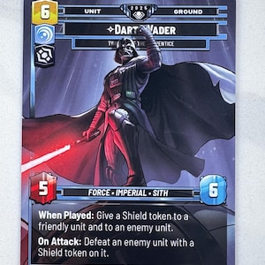 May include: A Star Wars trading card featuring Darth Vader. The card shows Darth Vader holding a red lightsaber, with text indicating his unit, force, and abilities. The card has a black and purple background.