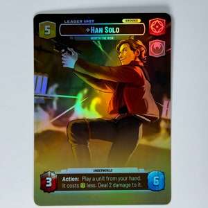 May include: A Star Wars collectible card game card featuring Han Solo, a leader unit with a cost of 5. The card has a gold background with a holographic effect. The card text reads "Action: Play a unit from your hand. It costs 1 less. Deal 2 damage to it."