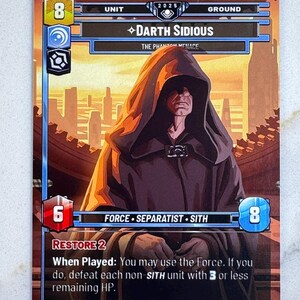 May include: A trading card featuring Darth Sidious from The Phantom Menace. The card has a brown background with a cityscape. Darth Sidious is depicted in a dark hooded robe. The card includes text such as "Force", "Sith", and "Restore 2".