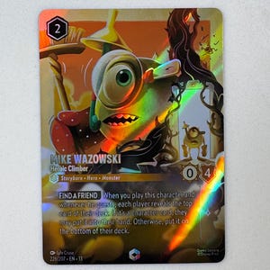 Könnte beinhalten: Eine holografische Disney Lorcana Sammelkarte mit Mike Wazowski als Heroic Climber. Die Karte zeigt die Figur mit einem Besen, den Text 'MIKE WAZOWSKI', 'Heroic Climber', 'Storyborn Hero Monster' sowie die Fähigkeit 'FIND A FRIEND'.