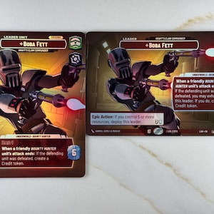 Puede incluir: Dos cartas coleccionables con Boba Fett del universo Star Wars. Las cartas muestran a Boba Fett en una pose dinámica, empuñando un arma con una explosión de energía roja. Las cartas tienen un esquema de color marrón y rojo con texto.