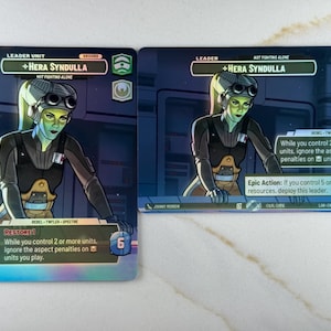 May include: Two trading cards featuring Hera Syndulla, a green-skinned character with a yellow ponytail, wearing a black uniform and goggles. The cards have text including "Leader Unit", "Leader", and "Restore 1". The background is a futuristic interior.