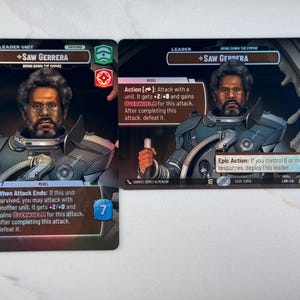 May include: Two trading cards featuring Saw Gerrera, a character from the Star Wars universe. The cards have a black background with text and graphics. One card has a 6 in a yellow box, and the other has a 7 in a blue box.