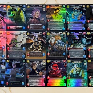 Puede incluir: Un conjunto de cartas coleccionables de Star Wars con varios personajes. Cada carta tiene un fondo holográfico e incluye arte de personajes, nombres y estadísticas del juego. Las cartas son de varios colores, incluyendo azul, verde y rojo.