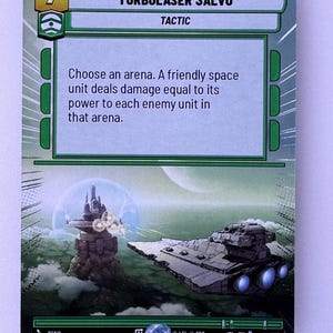 May include: A green and white Star Wars: The Card Game card with the text "TURBOLASER SALVO" and the number "7". The card is a tactic card and the text reads "Choose an arena. A friendly space unit deals damage equal to its power to each enemy unit in that arena."