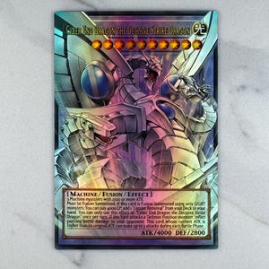 Peut inclure: Carte à collectionner holographique avec "Cyber End Dragon the Decisive Strike Dragon". La carte présente un design argenté et bleu avec une illustration détaillée d'un dragon mécanique. Le texte de la carte comprend ATK/4000 DEF/2800.