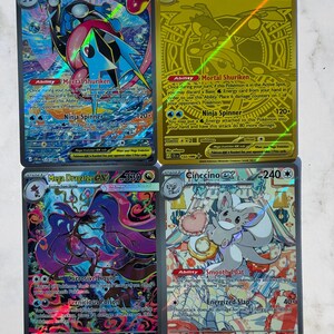 Può includere: Quattro carte collezionabili rettangolari con illustrazioni colorate di personaggi Pokemon. In alto a sinistra Mega Greninja EX, in alto a destra un Mega Greninja EX dorato, in basso a sinistra Mega Dragalge EX e in basso a destra Cinccino EX.