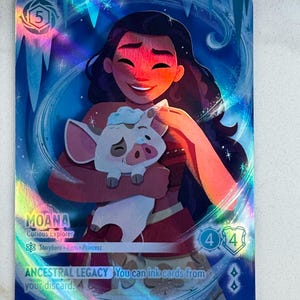 Peut inclure: Une carte à collectionner holographique représentant Moana, l'Exploratrice Curieuse, tenant un cochon. La carte a un fond bleu et blanc avec le texte "ANCESTRAL LEGACY" et d'autres détails du jeu. La carte est de la série Disney Lorcana.