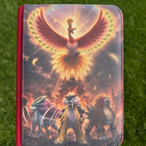 Puede incluir: Una carpeta rectangular con un estampado gráfico vibrante del Pokémon legendario Ho-Oh volando sobre Suicune, Raikou y Entei. La cubierta tiene una superficie texturizada con un lomo rojo brillante y esquinas redondeadas, mostrando un fondo ardiente.