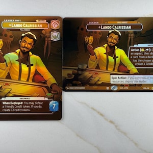 Puede incluir: Dos cartas de juego de cartas coleccionables con Lando Calrissian. Las cartas tienen un fondo marrón con una imagen amarilla y marrón de Lando. El texto en las cartas incluye "Leader Unit", "Full Sabacc" y "Underworld". Una carta tiene el texto "When Deployed: You may defeat a friendly Credit token."