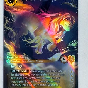 Könnte beinhalten: Eine Simba "King in the Making" Sammelkarte mit einer farbenfrohen Illustration von Simba. Die Karte hat eine goldene 7 in der oberen linken Ecke und zwei 5er in der oberen rechten Ecke. Der Kartentext enthält "Storyborn", "Hero", "Prince" und "Whisper".