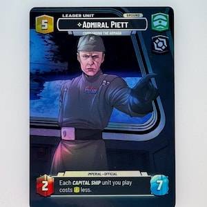 May include: A Star Wars: Armada card featuring Admiral Piett, a leader unit with a cost of 5. The card has a blue and black background with a picture of Admiral Piett in his Imperial uniform. The card text reads "Each Capital Ship unit you play costs 2 less."