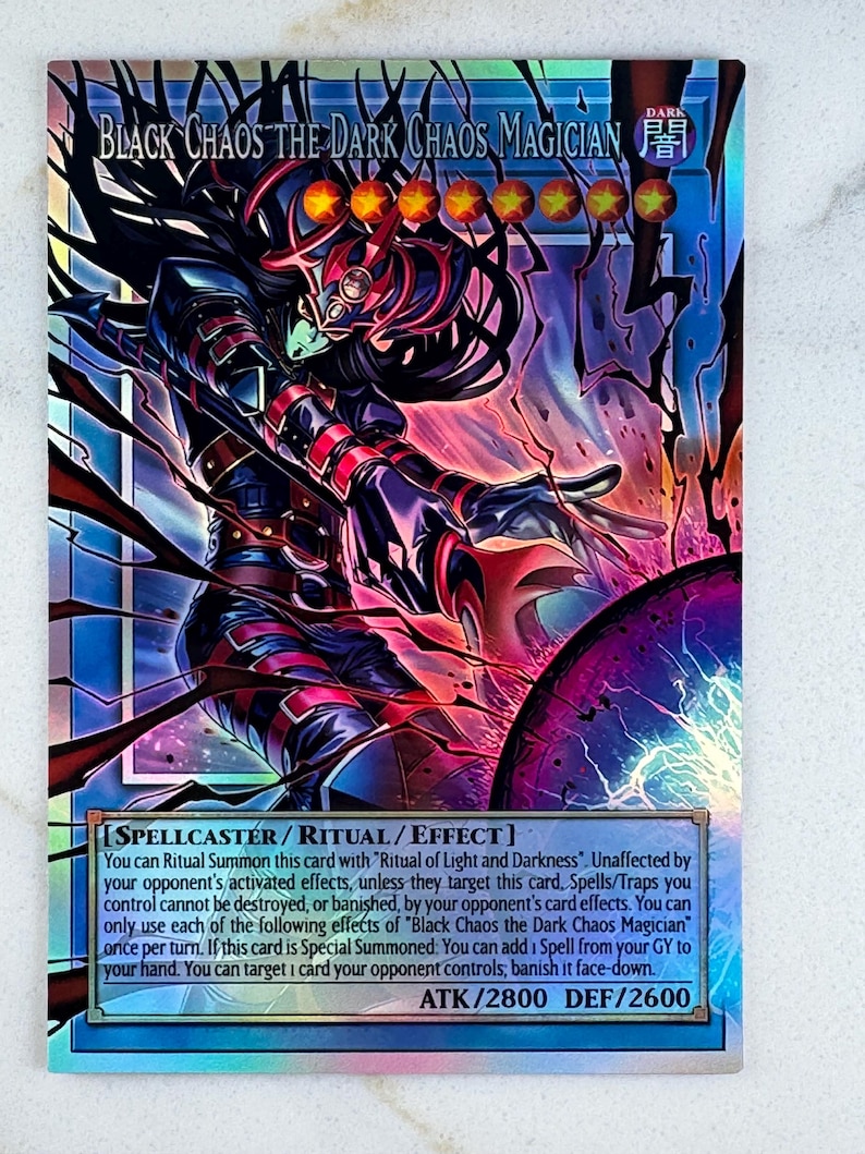 Puede incluir: Carta coleccionable hologr&aacute;fica con "Black Chaos the Dark Chaos Magician". La carta tiene un esquema de color oscuro con acentos rojos y negros. El texto de la carta incluye "SPELLCASTER / RITUAL / EFFECT" y ATK/2800 DEF/2600.