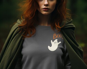 May include: A woman with long, curly red hair is wearing a gray sweatshirt with a white ghost graphic and the word "BOO." She is also wearing a green hooded cloak.