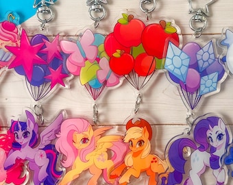 May include: A collection of colorful acrylic keychains featuring cartoon ponies and themed charms. Each keychain has a star-shaped clasp. The charms include rainbows, hearts, cupcakes, stars, butterflies, apples, gems, moons, and suns.