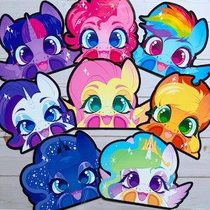Può includere: Una collezione di ritagli di facce di pony dei cartoni animati colorati. Ogni pony ha grandi occhi e un'espressione sorridente. I pony includono personaggi rosa, blu, viola, gialli e arancioni con vari colori e stili di capelli.
