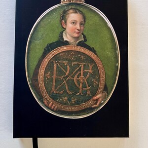 May include: Black notebook featuring a portrait of a woman within a silver-colored frame. The portrait has a green background and a decorative crown. The notebook includes a black ribbon bookmark.