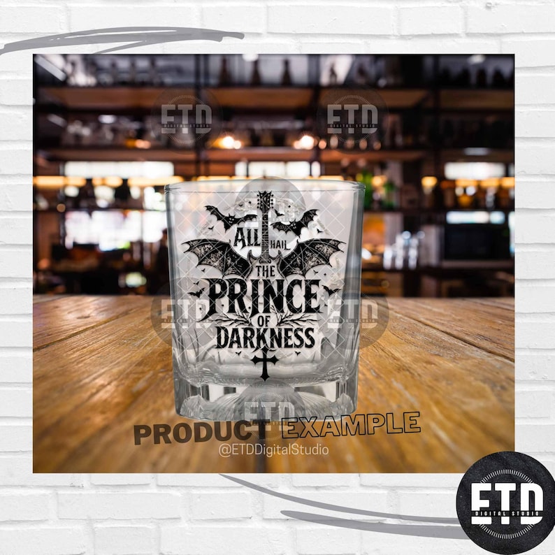 Puede incluir: Un vaso de whisky transparente y cuadrado con el texto "ALL HAIL THE PRINCE OF DARKNESS" en fuente g&oacute;tica, junto con ilustraciones de murci&eacute;lagos y guitarra. El vaso est&aacute; sobre una superficie de madera.