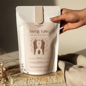 Può includere: Busta bianca di "Energy Tonic", un'alternativa adattogena al caffè. L'etichetta è marrone chiaro con il nome del marchio in alto. L'etichetta presenta due figure con un chicco di caffè al centro. La busta è tenuta in mano.