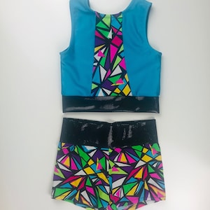 May include: A two-piece athletic outfit with a sleeveless crop top and shorts. The top is turquoise blue with a black mesh waistband and a geometric pattern on the back. The shorts are black with a geometric pattern in bright colors, including pink, yellow, green, and blue.