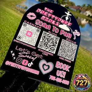 May include: Black and pink sign with the text "The Prettypuff Girls" and "Scan to Pay". The sign includes QR codes for Cashapp, Blinq, Zelle, and a business card. It also includes the text "Let's Get Social!" with social media icons and the text "Book Us!" with a phone number.