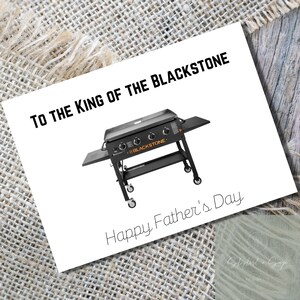 Puede incluir: Una tarjeta blanca con texto negro que dice "To the King of the Blackstone. Happy Father's Day."  Se muestra una plancha Blackstone negra con texto naranja en la tarjeta.