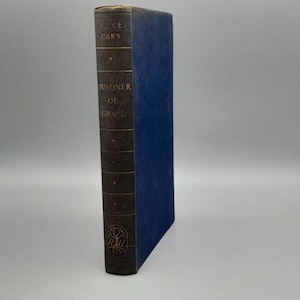 Puede incluir: Un libro de tapa dura azul con letras doradas en el lomo. El título es "Prisoner of Grace" de Joyce Cary.