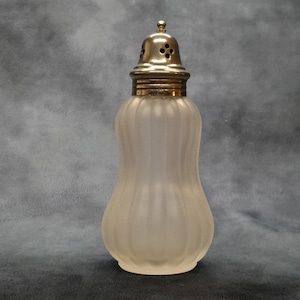 May include: A vintage frosted glass salt shaker with a silver-coloured metal top. The shaker has a bulbous body with vertical ribbed detailing. The top features a perforated design for dispensing salt.
