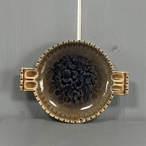 May include: A brown and cream ceramic dish with a floral design. The dish has two handles on the sides.