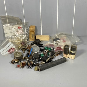 May include: A collection of vintage electronic components, including resistors, capacitors, switches, and potentiometers. The components are in various colours, including green, black, and red. Some of the components are in clear plastic containers.