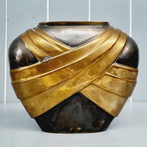 May include: A decorative vase with a dark brown body and gold bands wrapped around it.