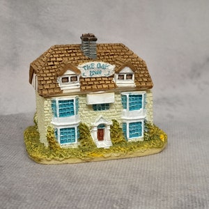 May include: A miniature model of a white brick building with a brown roof. The building has blue windows and a sign that reads "The Oak Inn".