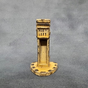 Può includere: Un piccolo segnale stradale in metallo giallo usurato con la scritta "KEEP LEFT" in lettere nere. Il segnale ha un corpo rettangolare e una base circolare con dettagli neri. Il design suggerisce un'estetica vintage o antica.