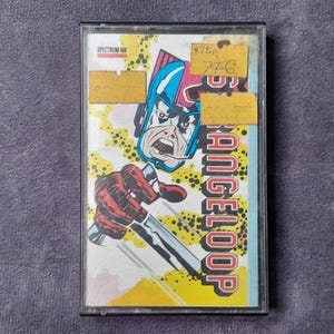 May include: Vintage cassette tape featuring comic book art. The cover art depicts a character with a blue helmet and red gloves, holding a metallic object. The title "ANGELOOP" is visible. Includes yellow price tags.