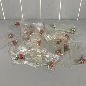 May include: A pile of small, red, electronic toggle switches in clear plastic bags.