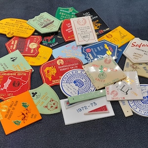 Può includere: Una collezione di distintivi da rally vintage in varie forme e colori. I distintivi presentano testo e grafica, inclusi gli anni 1970, 1972 e 1977. Alcuni distintivi riportano le parole "Safari" e "Trailer Caravan Club."