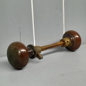 May include: A vintage door knob with two brown wooden knobs and a brass connecting rod.