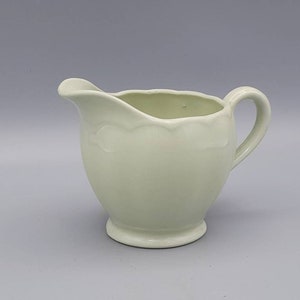 May include: A pale green ceramic jug with a fluted rim and a rounded body. The jug has a handle on the side and a smooth, glossy finish.