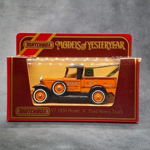 May include: Matchbox Y7 1930 Model "A" Ford Wreck Truck toy in its original box. The orange and black truck has white-walled tires and a tow crane. The box is red and gold with the Matchbox logo and "Models of Yesteryear" text.