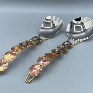 May include: A set of two silver serving utensils with brass handles and copper accents. The handles are decorated with a series of round copper discs.