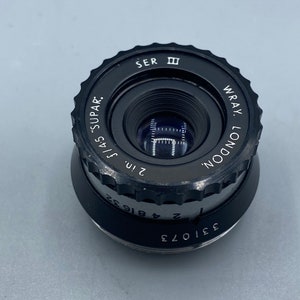 Pu&ograve; includere: Un obiettivo nero Wray London da 2 pollici f/4.5 "Supar" con un anello di apertura argentato e un tappo dell'obiettivo nero.