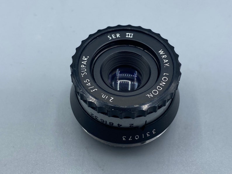 Pu&ograve; includere: Un obiettivo nero Wray London da 2 pollici f/4.5 "Supar" con un anello di apertura argentato e un tappo dell'obiettivo nero.