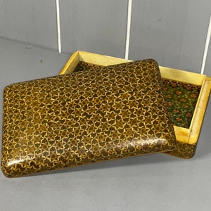 Puede incluir: Una caja de madera con un patrón geométrico en la tapa y en el interior. La caja está hecha de madera y tiene un color marrón claro. El patrón está hecho de pequeños trozos de madera que están incrustados en la superficie de la caja.