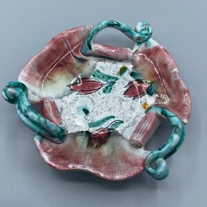 Puede incluir: Un pequeño plato de cerámica con un borde festoneado y tres asas. El plato está decorado con un patrón floral en tonos de rosa, verde y blanco.