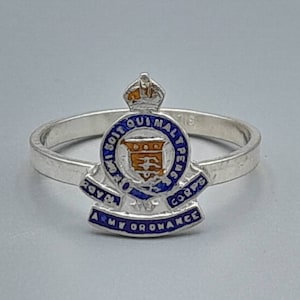 May include: A silver ring with a blue and gold enamel design. The design features a crown, a shield, and the words "Royal Army Ordnance Corps".